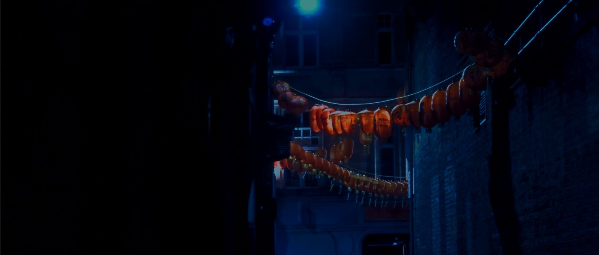 Red paper lanterns strung across a dark Chinatown street, lit from a blue doorway