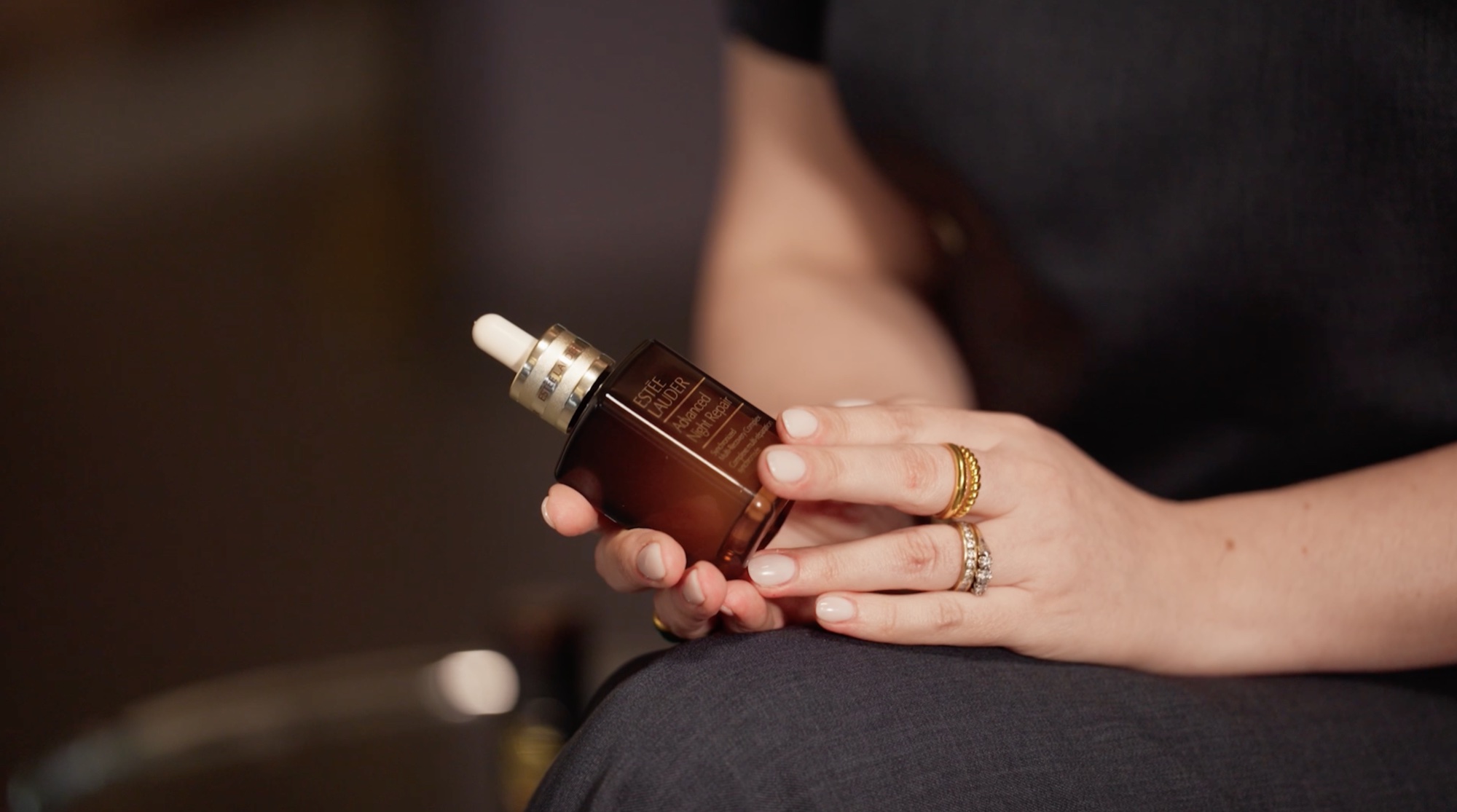 Hands holding the Advanced Night Repair bottle, gold rings catching the light