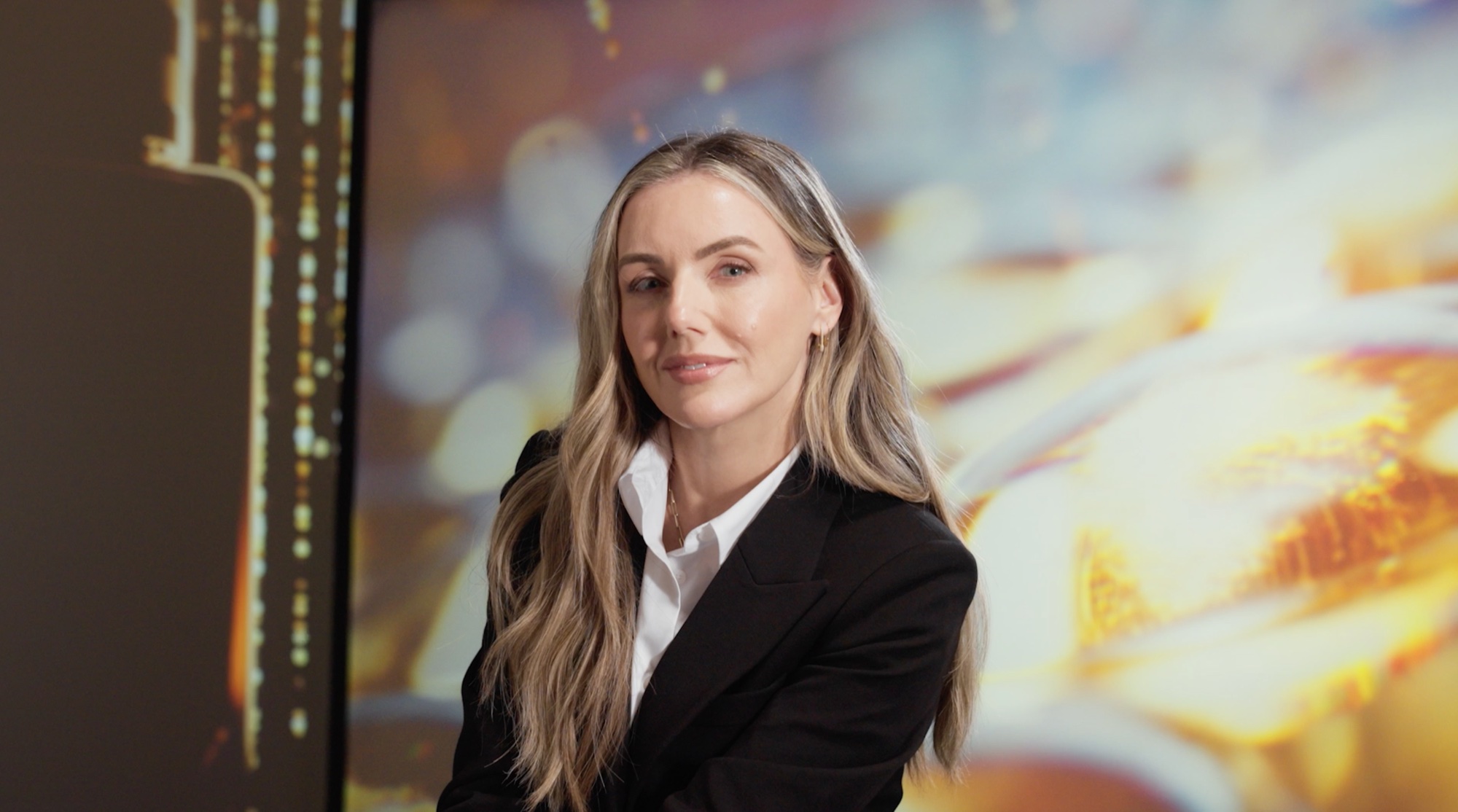 Talent in a black blazer looking to camera, projected bokeh behind her