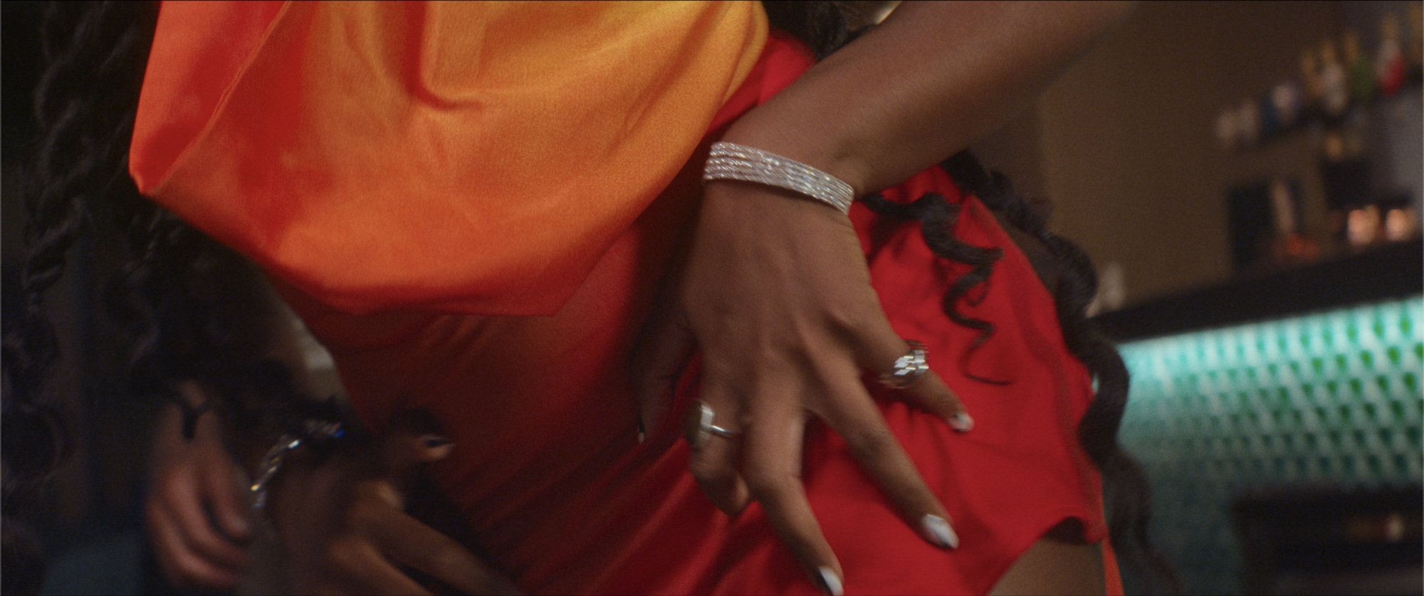 Close on hands and a red dress at the bar, rings and a diamond bracelet