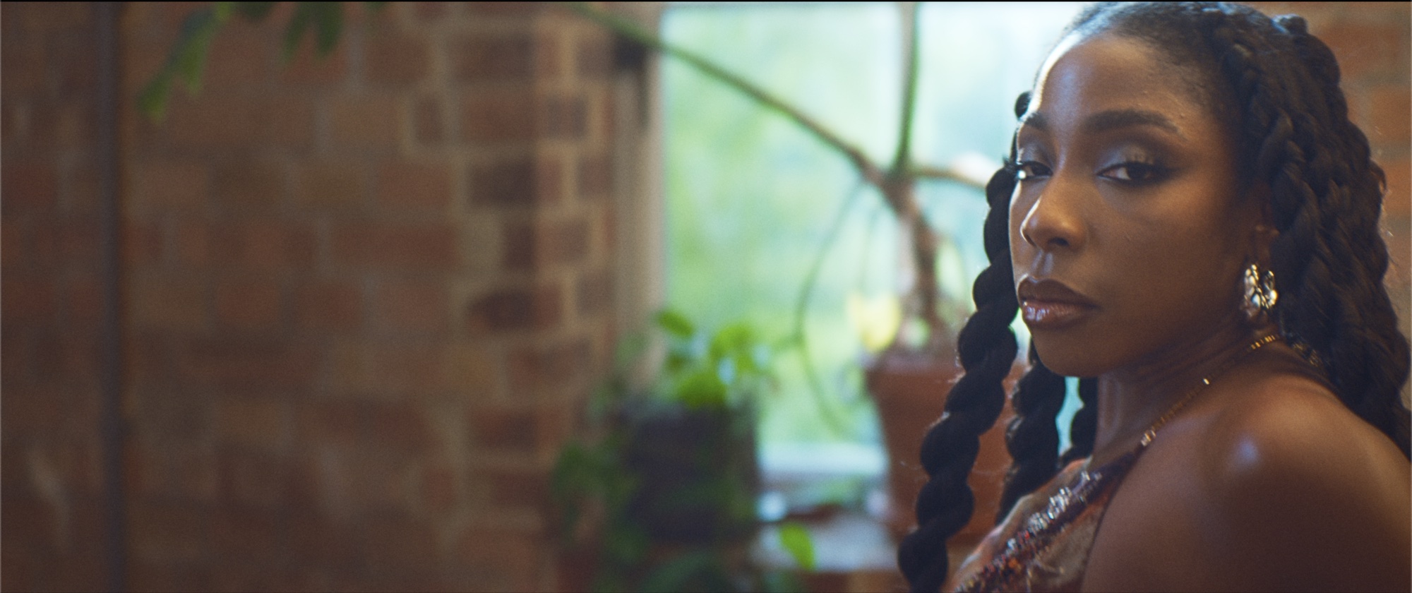 Nissi in profile in the loft, braids and gold jewellery in soft window light