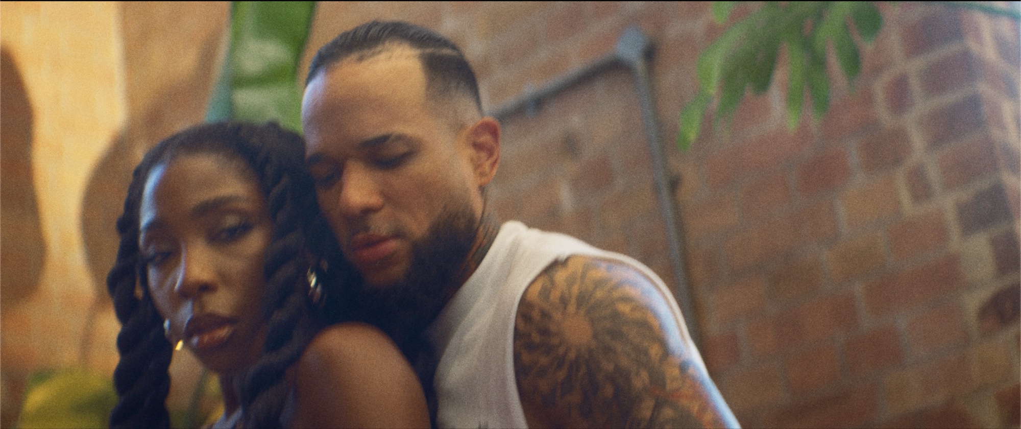 Nissi and a man in a close embrace against the brick wall