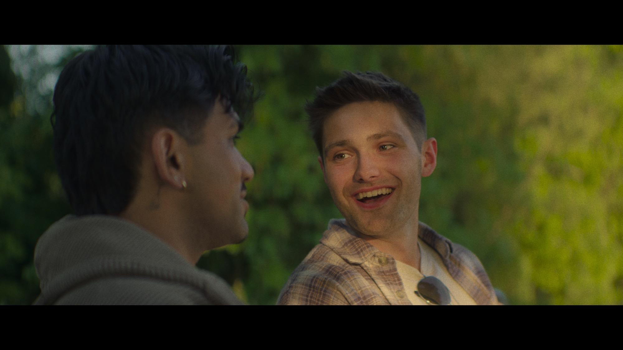 Two friends laughing in soft daylight against greenery