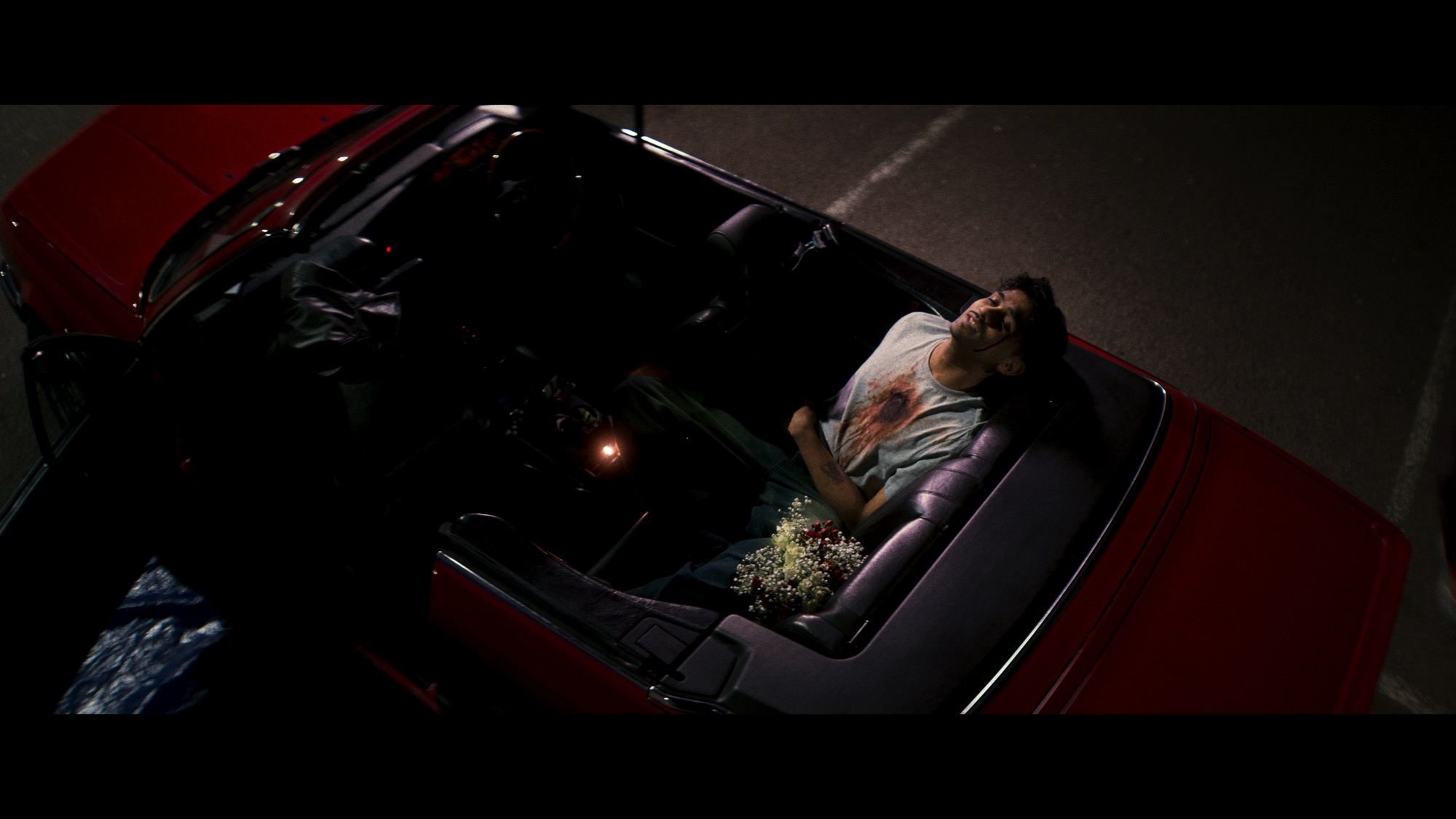 Top-down of a man lying in the back of a red convertible with flowers