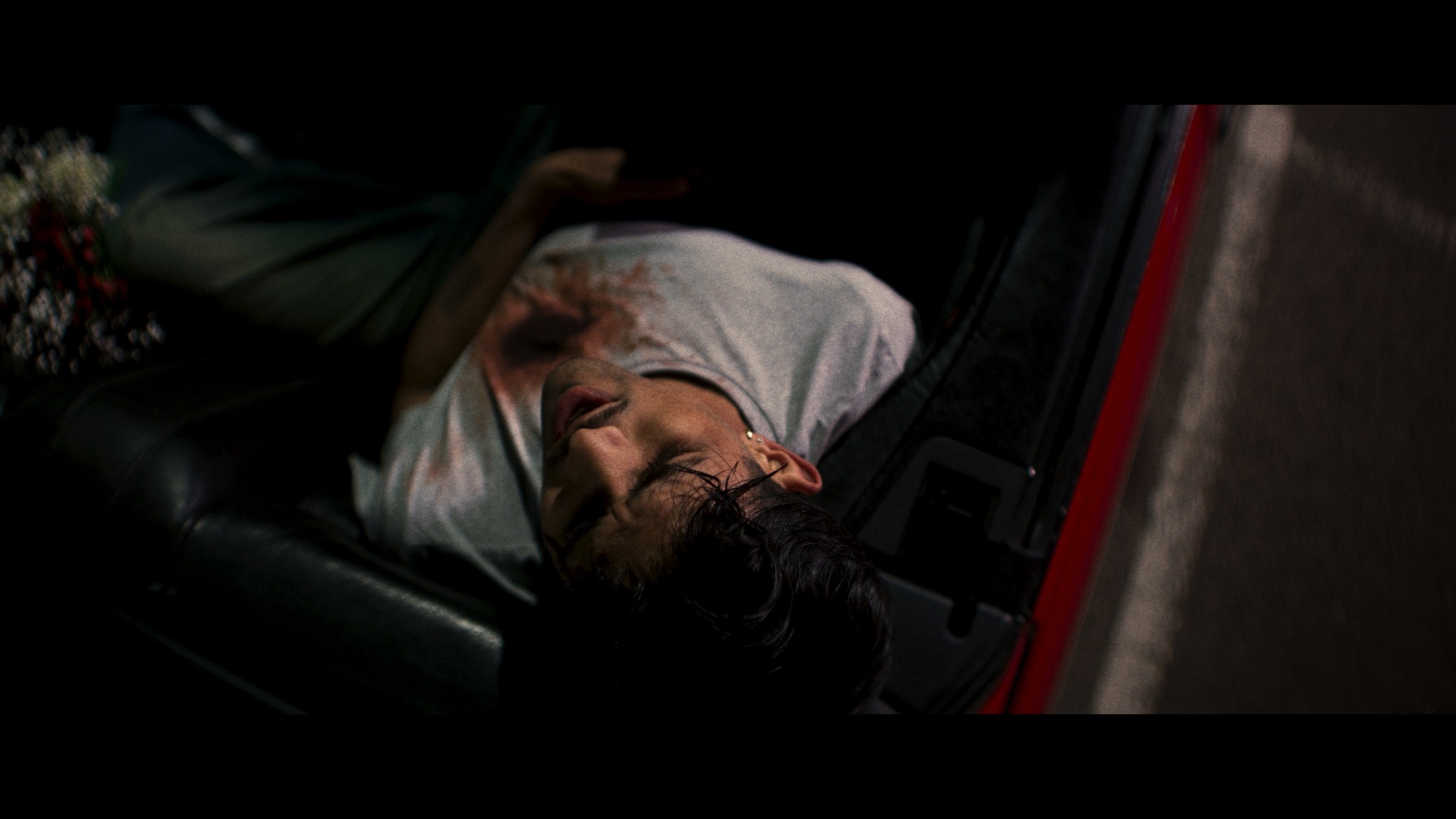 Close on a man asleep in the red convertible, flowers beside him