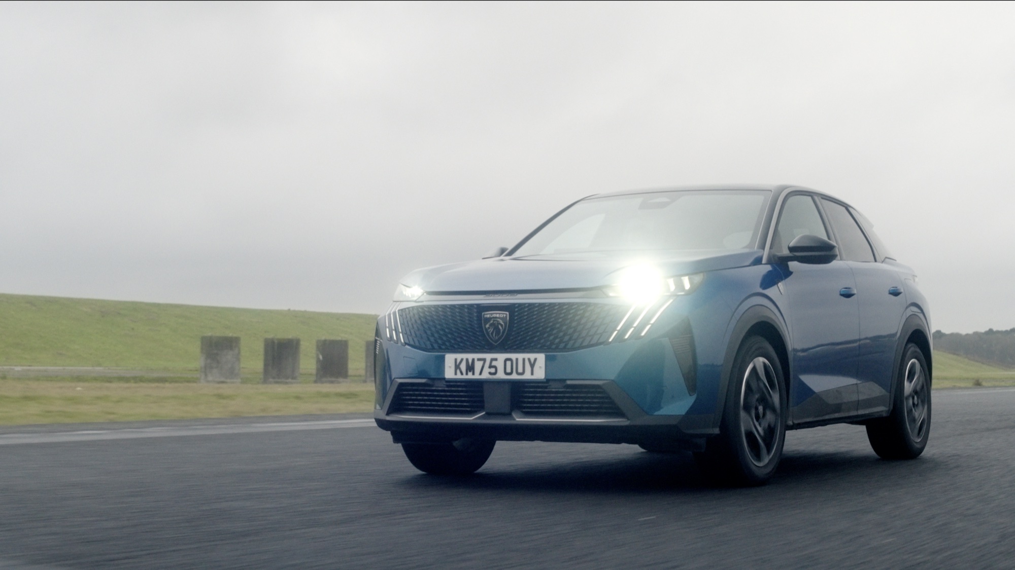 Blue Peugeot 3008 on the runway with its lights on under a low grey sky
