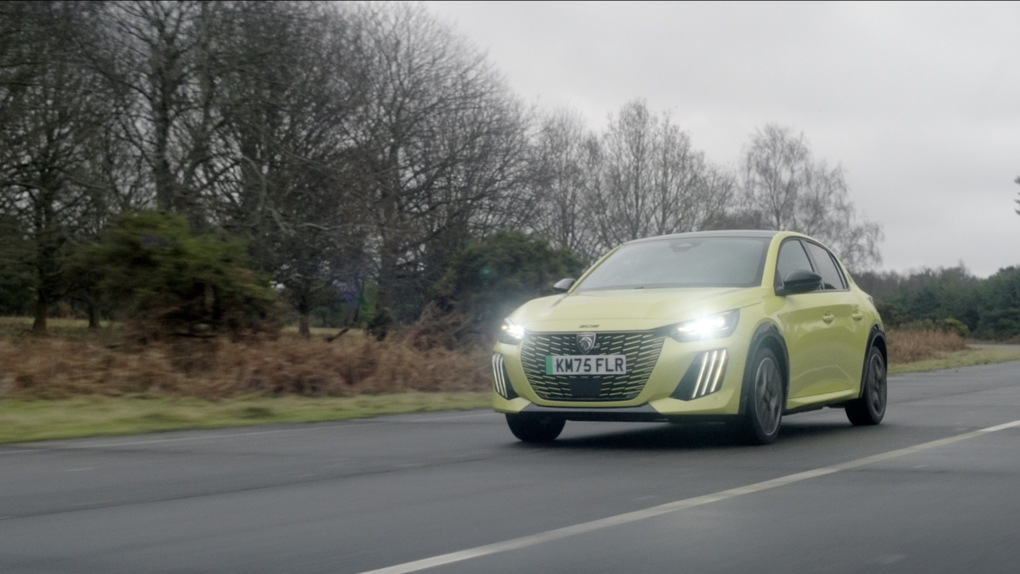 Yellow Peugeot 208 driving past a treeline