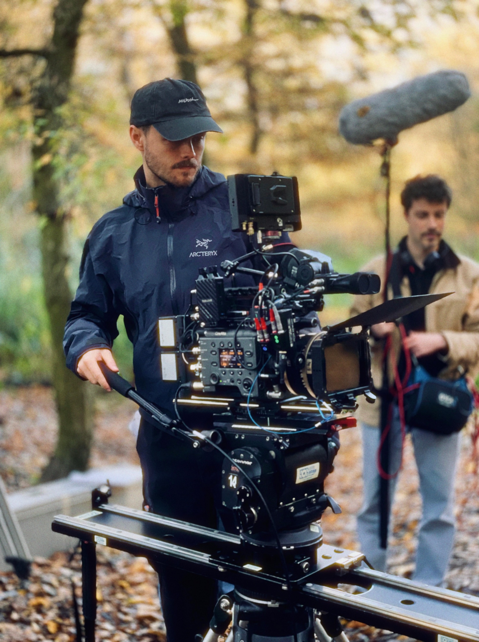 Oliver Durnford at the eyepiece of a Sony VENICE on a slider in autumn woodland, boom operator behind