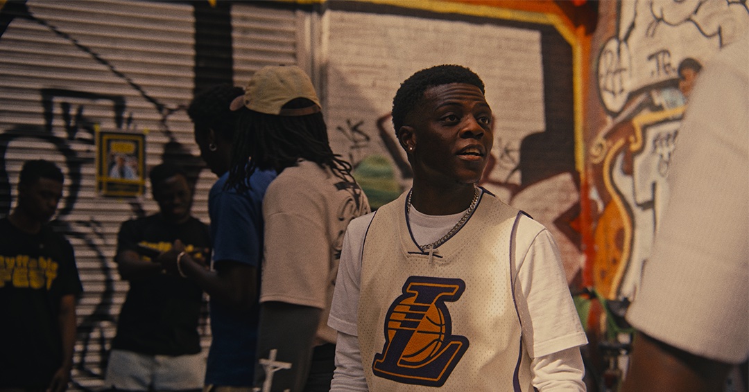 Man in a Lakers jersey with a crowd against a graffiti wall