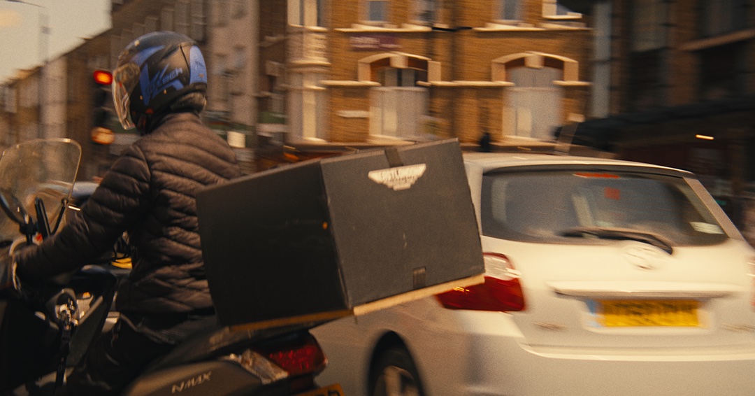 Delivery rider passing a white car on a London street