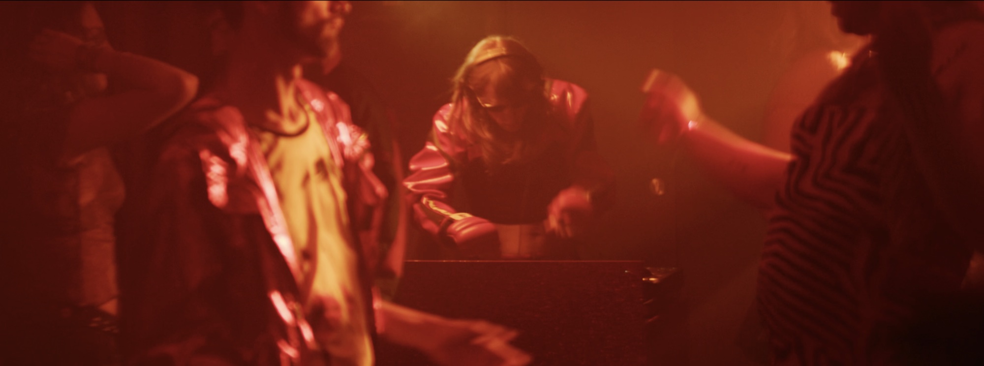 Crowd in a red-lit room, figures blurring past the camera