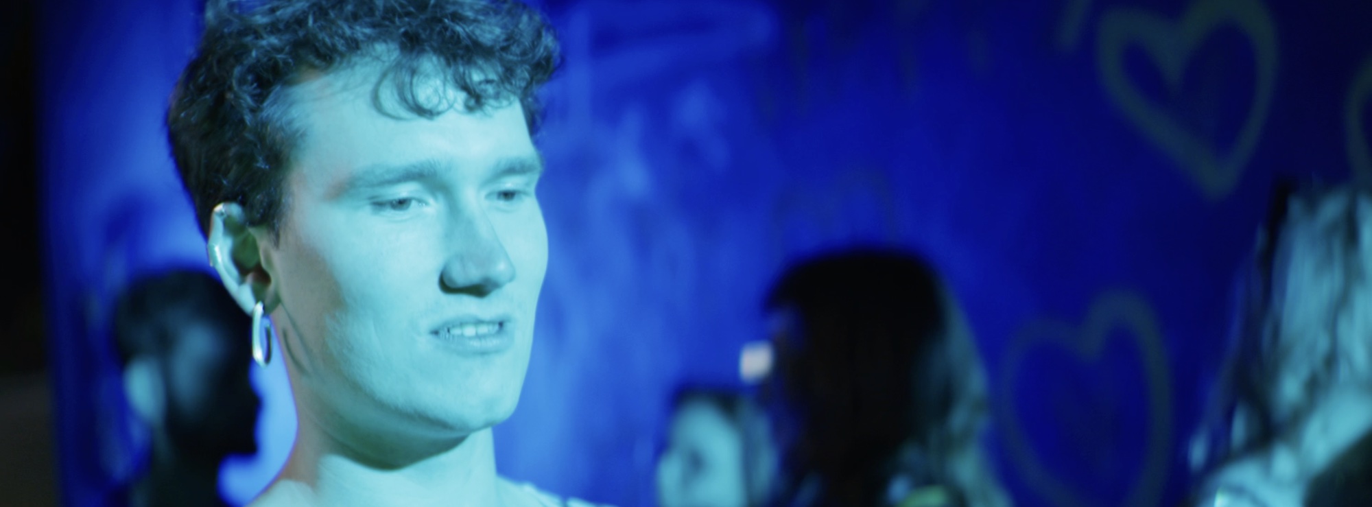 Performer in blue light in front of graffiti hearts
