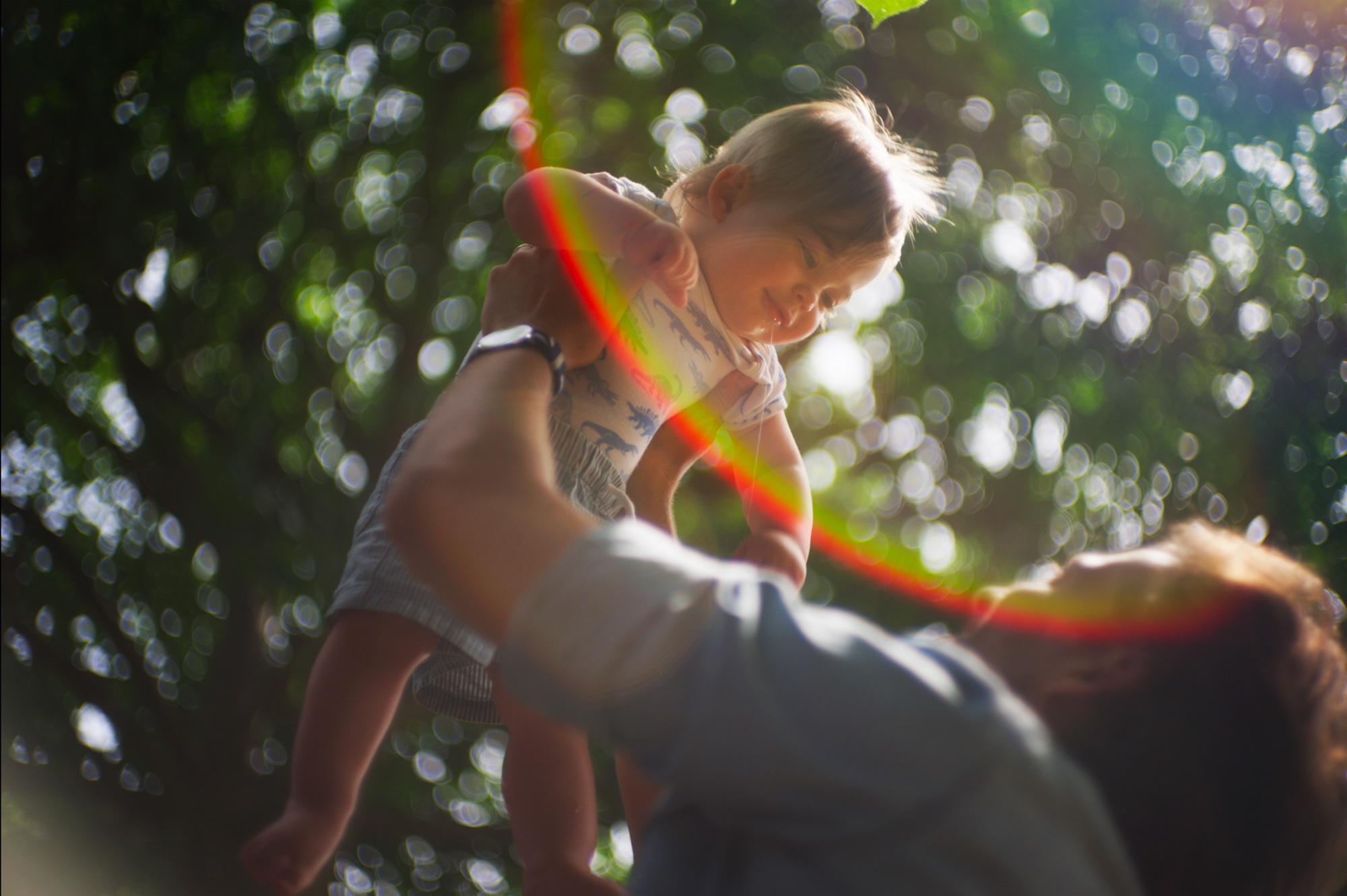 A child lifted into dappled sunlight with a rainbow lens flare, from the short film 'The Forgotten'